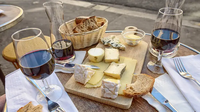 A table set with a cheese board, bread basket and glasses of red wine.