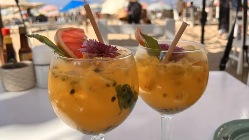 Two fruity cocktails garnished with grapefruit at a sunny beach bar.
