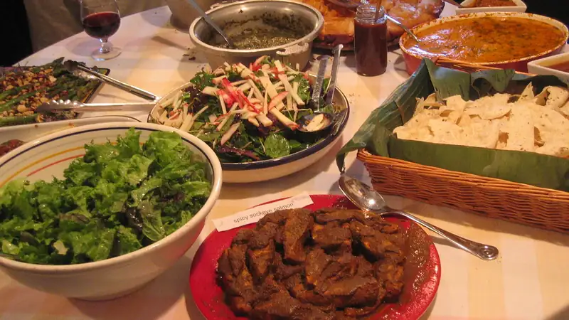 A potluck table crowded with salads, casseroles and serving dishes.