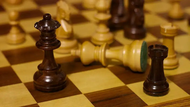 Wooden chess pieces on a board mid-game, with one piece toppled on its side.