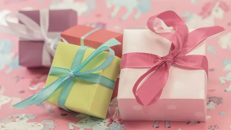 A pile of small wrapped gift boxes tied with pink, blue and white ribbons on patterned paper.