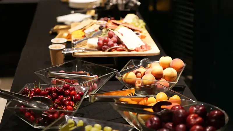 A buffet table with bowls of cherries, peaches, grapes and a cheese board.