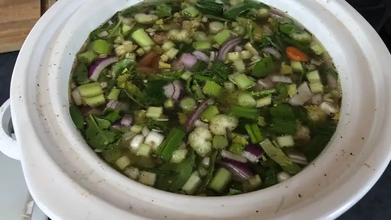 A slow cooker filled with chopped vegetables and broth.