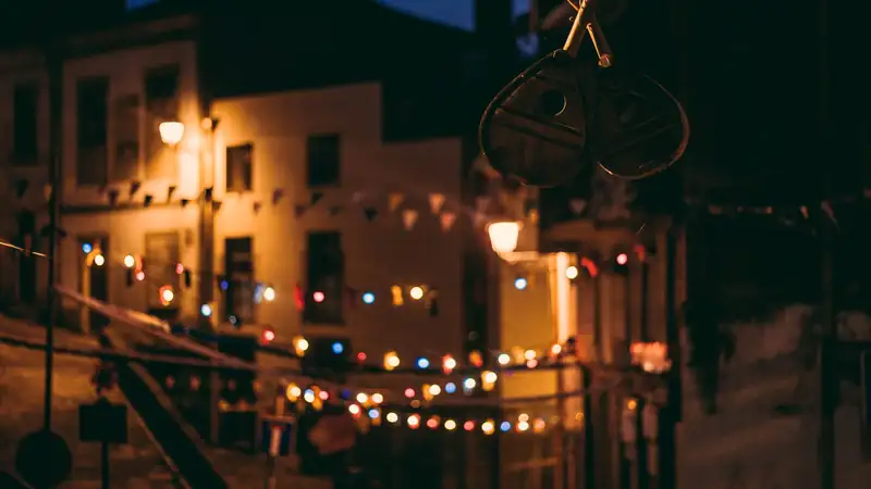 Strings of colorful bulbs hung across a narrow old-town street at night during a summer festival.
